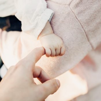 A baby being held and holding on to an adult's finger.